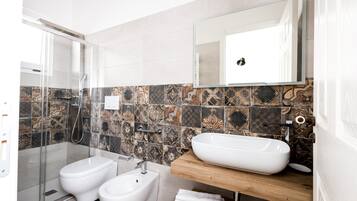 Un baño moderno con cabina de ducha de vidrio, un bidé, un lavabo con encimera de madera y un espejo sobre el lavabo.