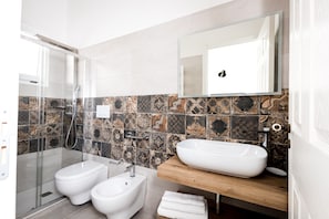 Un baño moderno con cabina de ducha de vidrio, un bidé, un lavabo con encimera de madera y un espejo sobre el lavabo.