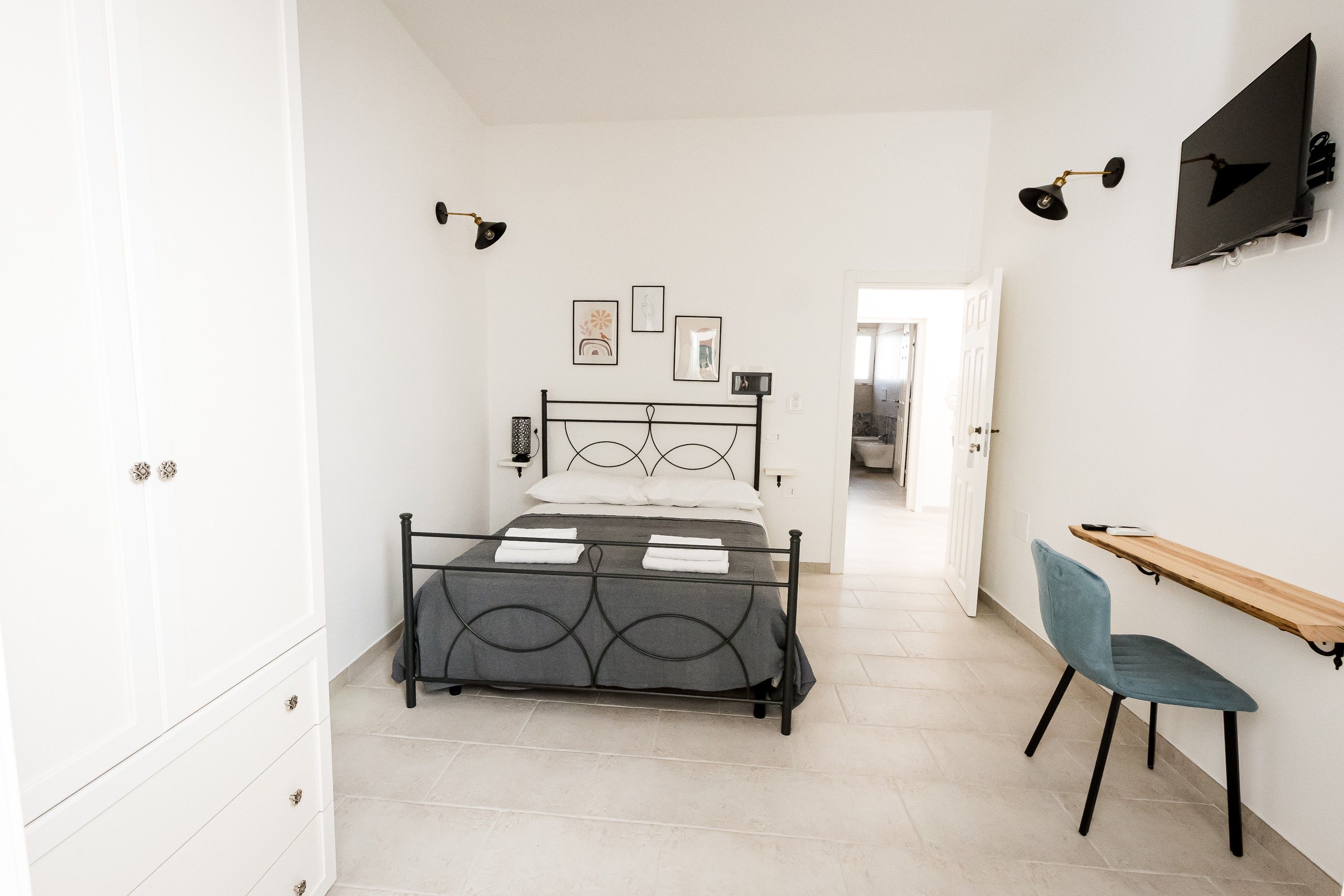 Une chambre à coucher avec un lit, un bureau et une chaise. Des lampes murales et des tableaux ornent les murs.