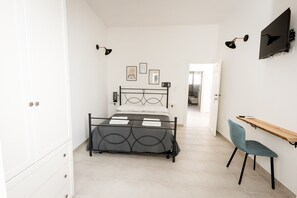 Ein Schlafzimmer mit Bett, Schreibtisch und Stuhl. An den Wänden sind Lampen und Bilder angebracht.