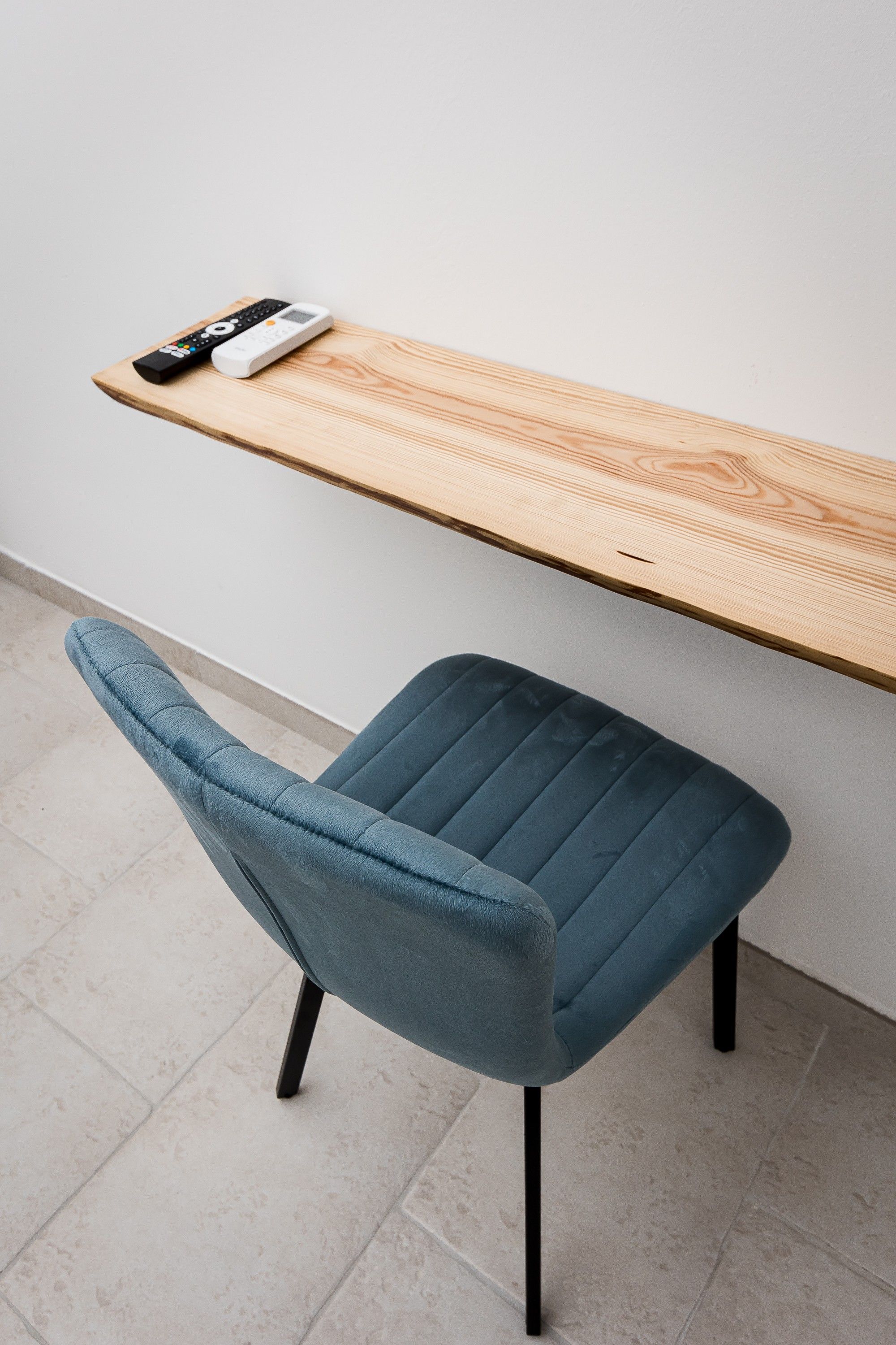 Una silla moderna con asiento y respaldo de tela oscura, junto a un escritorio de madera y un control remoto.