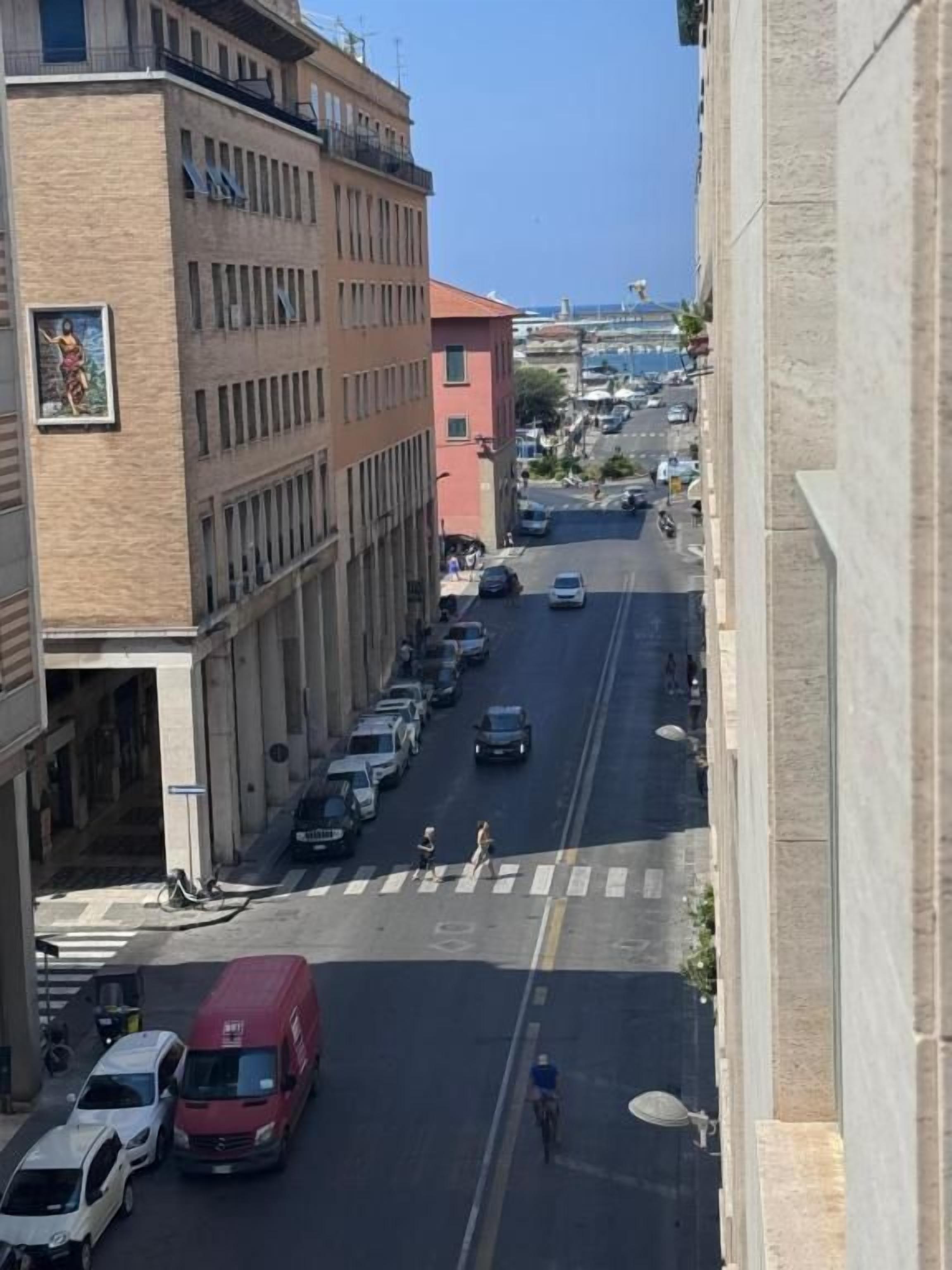Straßenansicht mit Gebäuden, parkenden Autos und einer Fußgängerampel.