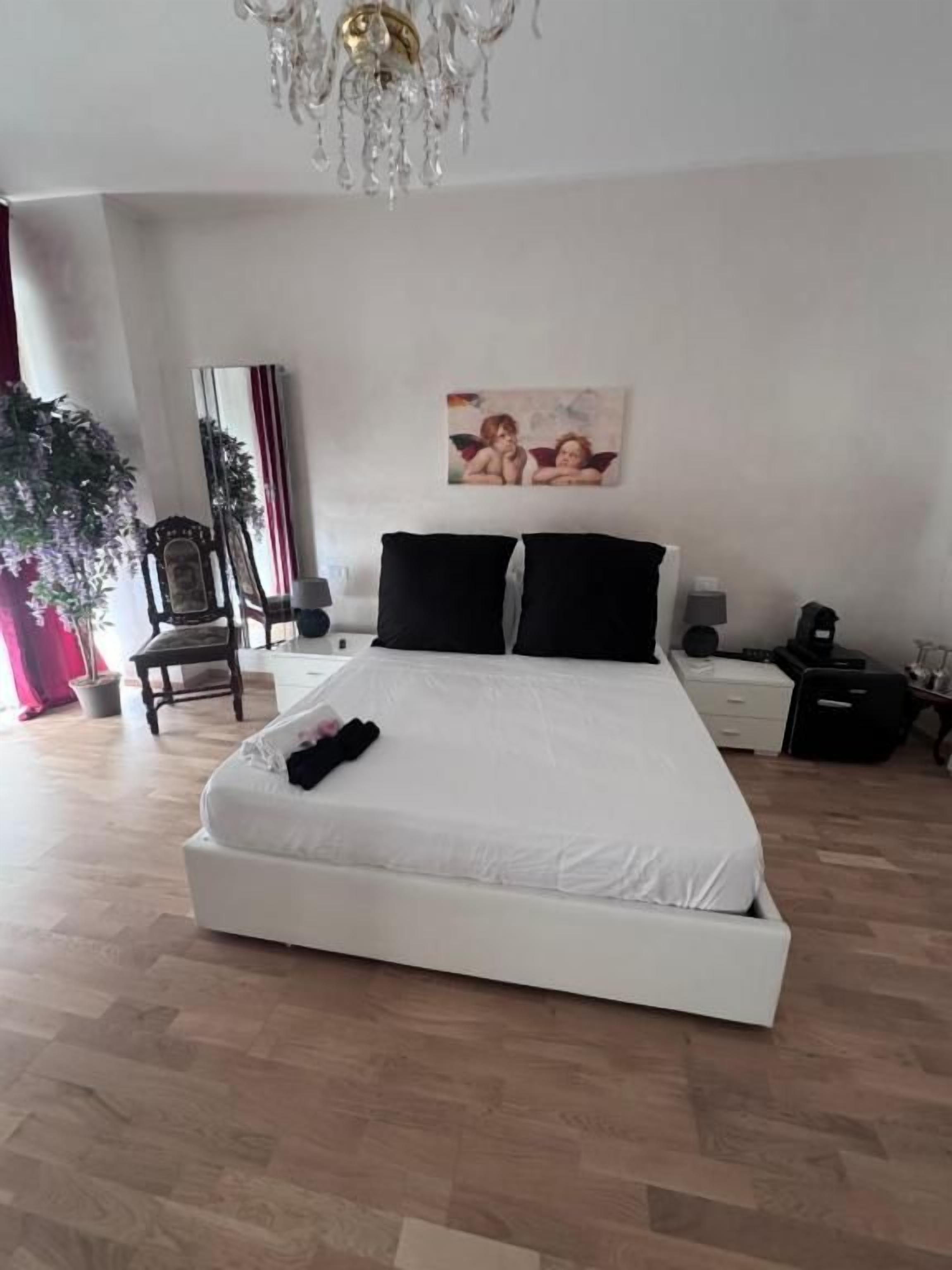 Un dormitorio con una cama blanca, un candelabro, un cuadro en la pared y una planta en maceta.