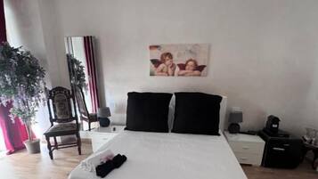 Un dormitorio con una cama blanca, un candelabro, un cuadro en la pared y una planta en maceta.