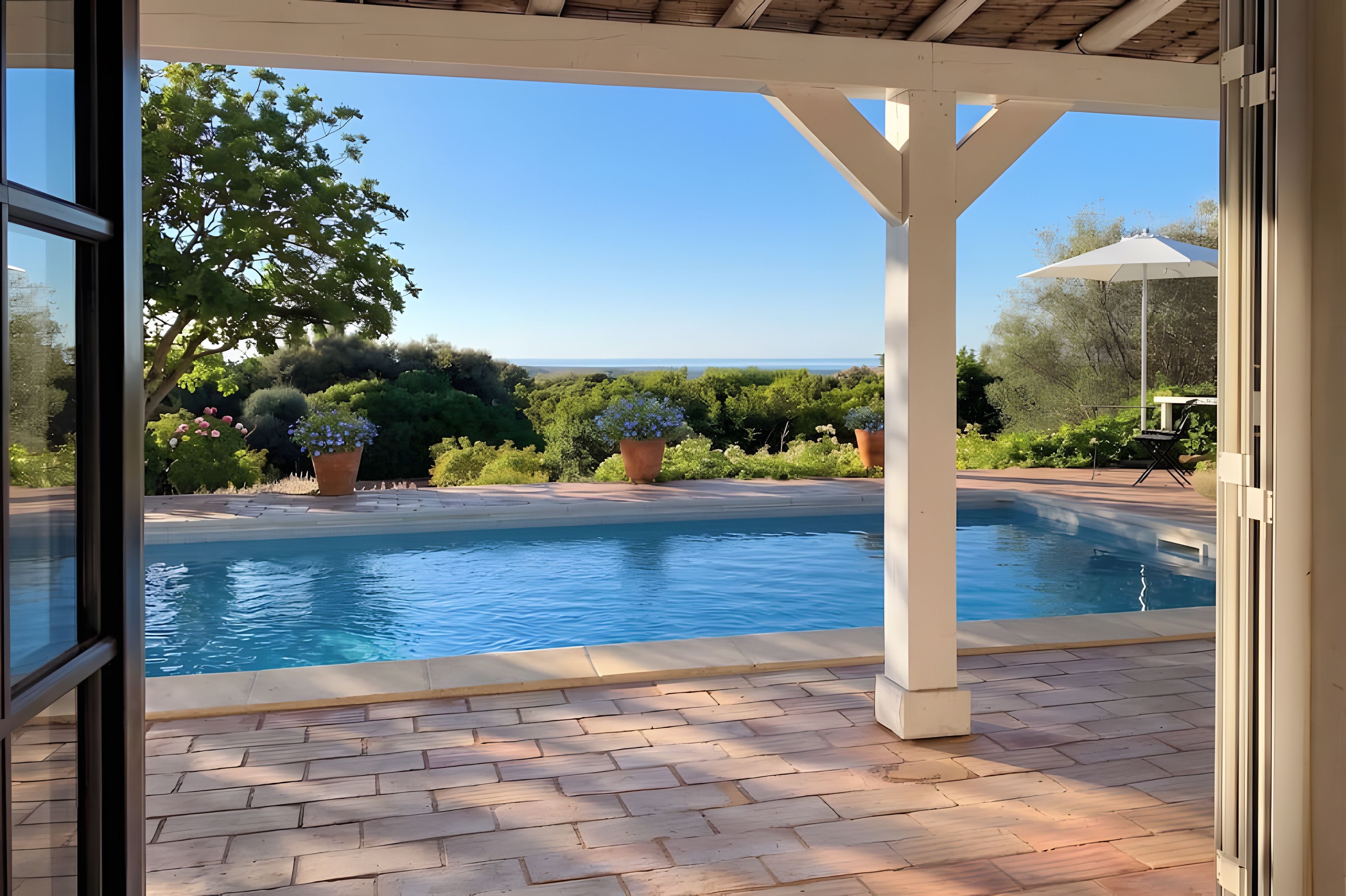 A pool area with a clear view of the sea, surrounded by potted plants and a pergola structure.