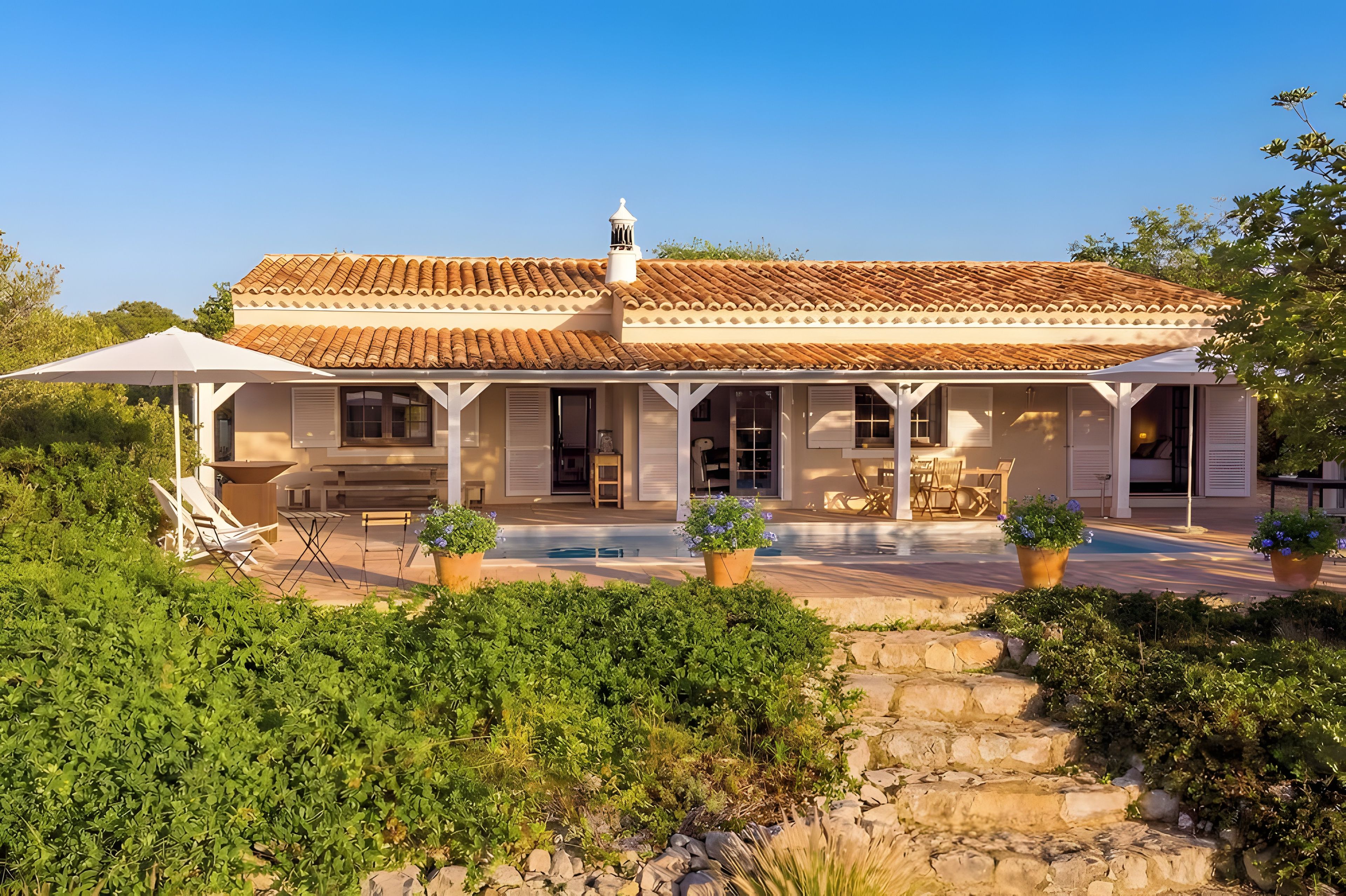 A two-story house with a tiled roof, a covered patio area with outdoor furniture, and a stone pathway leading to the entrance.