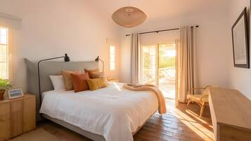 Un dormitorio con cama, mesitas de noche, lámpara, una silla y vista al exterior.