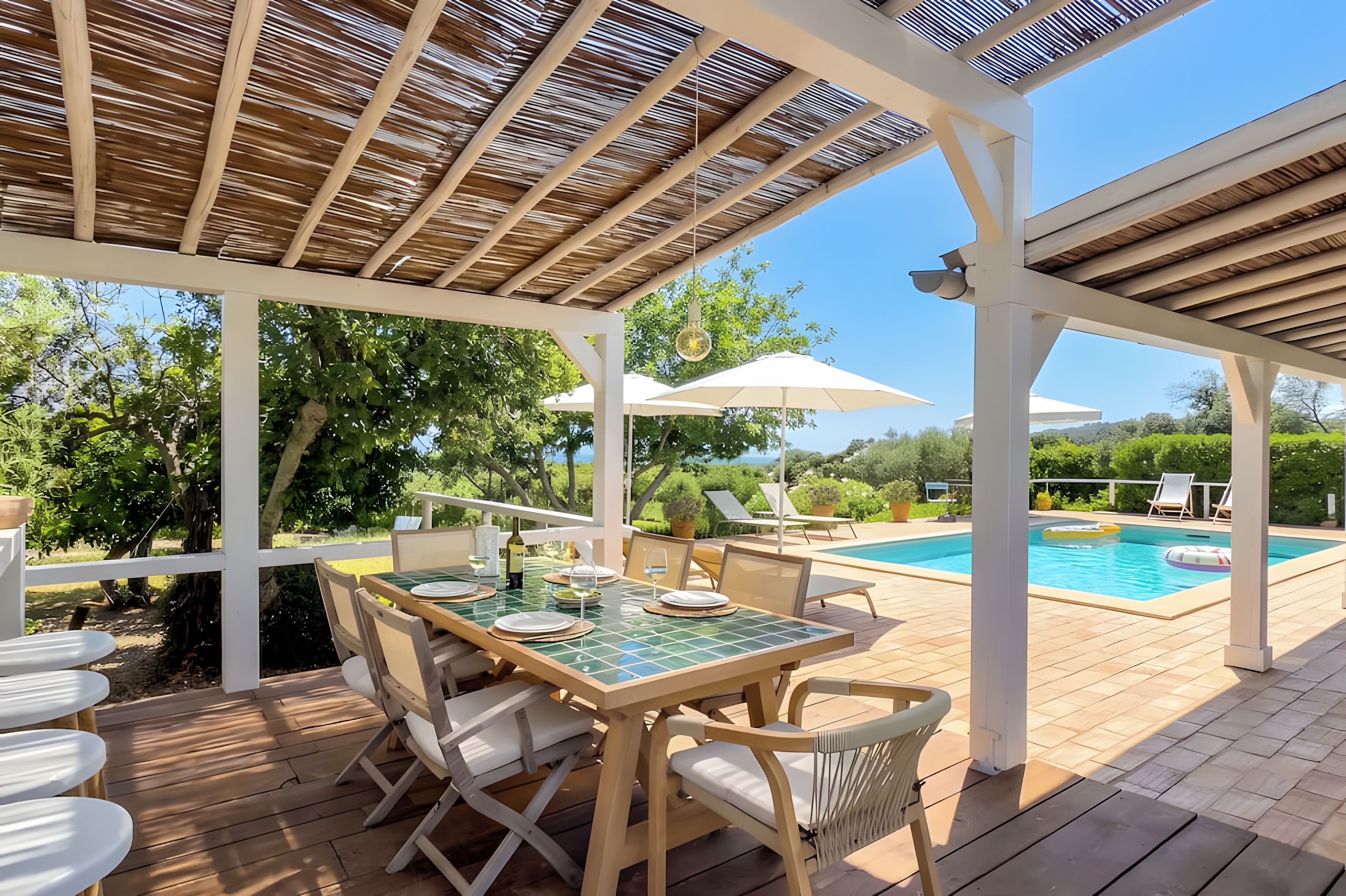 A covered outdoor area with a pool, wooden deck, and a table set for dining.
