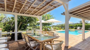 A covered outdoor area with a pool, wooden deck, and a table set for dining.