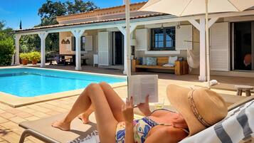 A poolside area with a lounge chair, a covered patio, and a pool.