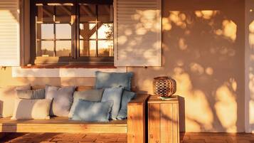 A wooden bench with cushions, a small table with a lantern, and a window with shutters.