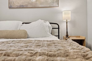 A neatly made bed with white linens and a beige throw blanket, a bedside lamp, and a framed artwork on the wall. - Beautiful Modern 3BR Home w/ Spacious Living Area (Buffalo Gap)
