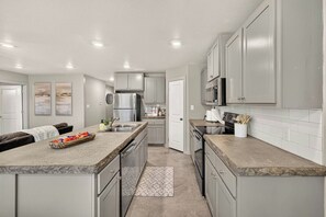 A modern kitchen with grey cabinetry, stainless steel appliances, and a marble countertop. - Beautiful Modern 3BR Home w/ Spacious Living Area (Buffalo Gap)