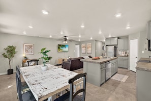 A modern kitchen with grey cabinets, a central island, and a dining area with a rustic table. - Beautiful Modern 3BR Home w/ Spacious Living Area (Buffalo Gap)