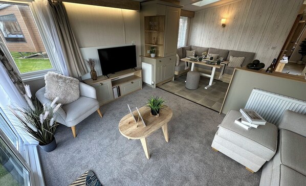 A modern living room with a flat-screen TV, a sofa, a coffee table, and a dining area with a table and chairs.