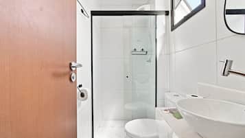 Ein modernes Badezimmer mit einer Duschkabine aus Glas, einer weißen Toilette und einem großen, weißen Waschbecken.