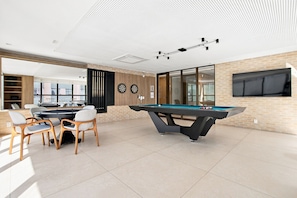 Espaço de lazer moderno em ambiente interno, com mesa de bilhar, dardos e sinuca.