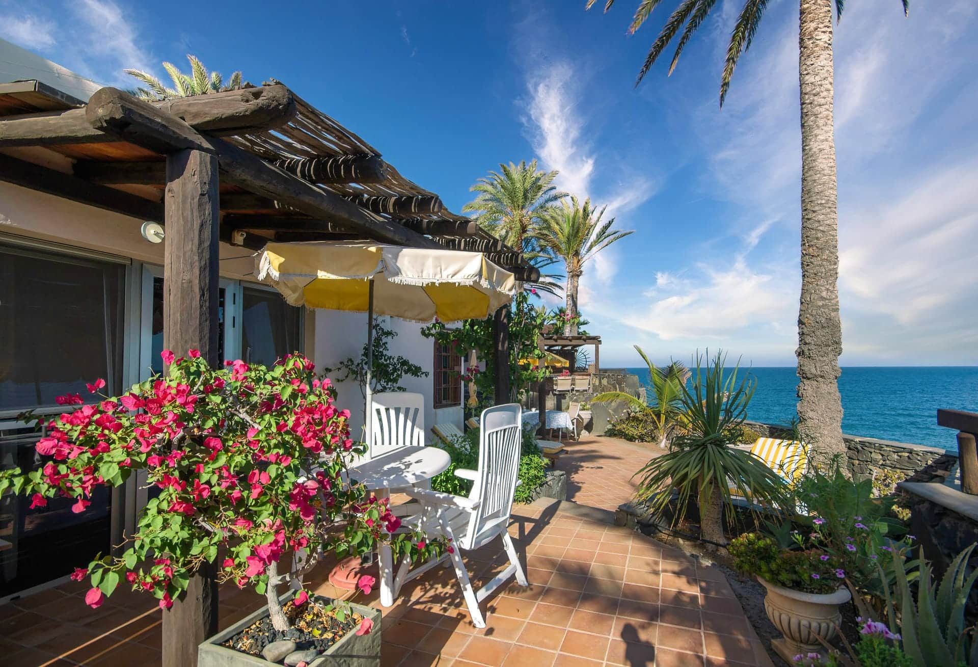 Un patio con mesa y sillas, una pérgola de madera y vista al mar.