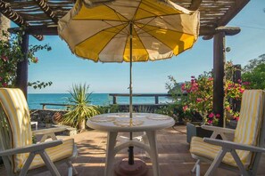 Um pátio com uma mesa, duas cadeiras, um guarda-sol e vista para o mar.