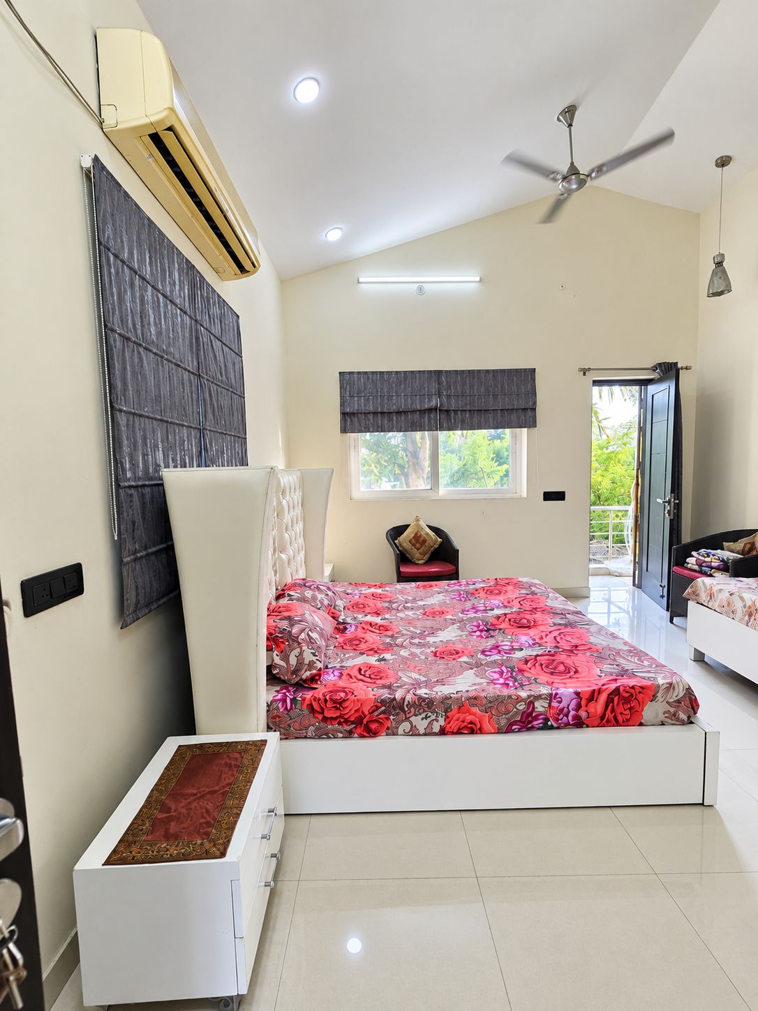 A bedroom with a bed, a ceiling fan, a window with a view, and a door leading outside.