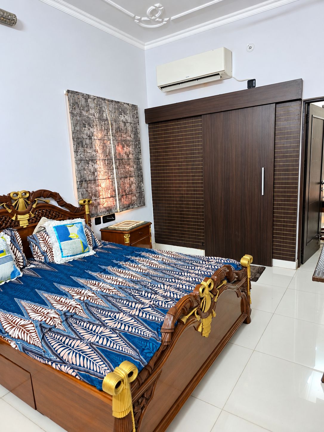 A bedroom with a wooden bed, a wardrobe, an air conditioning unit, and a large abstract painting.