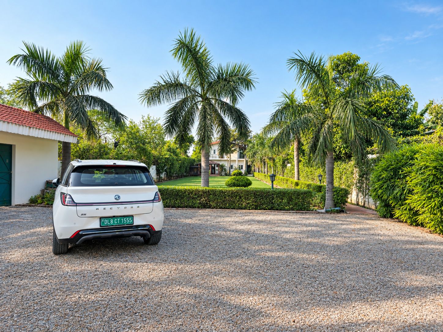 A white car parked in a gravel driveway with a house and palm trees in the background.