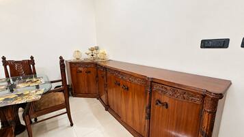 A dining area with a glass-top table, wooden chairs, and a wooden cabinet with ornate carvings.