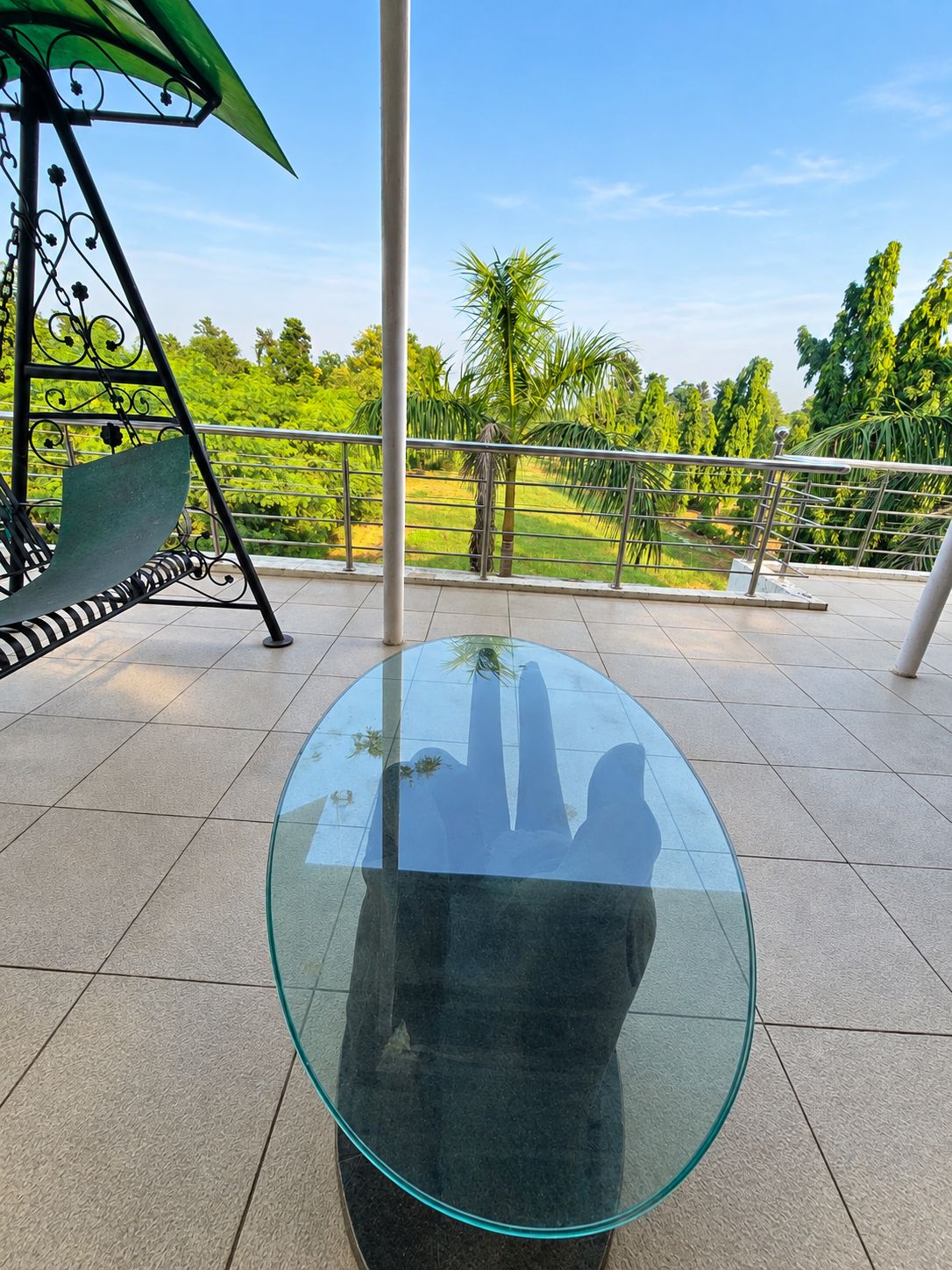 A glass-top table on a balcony with a metal railing and a green bench.
