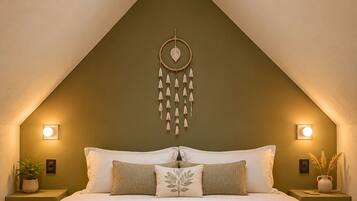 Un dormitorio con techo inclinado, una cama con ropa blanca, una decoración de atrapasueños y luces fijadas a la pared.