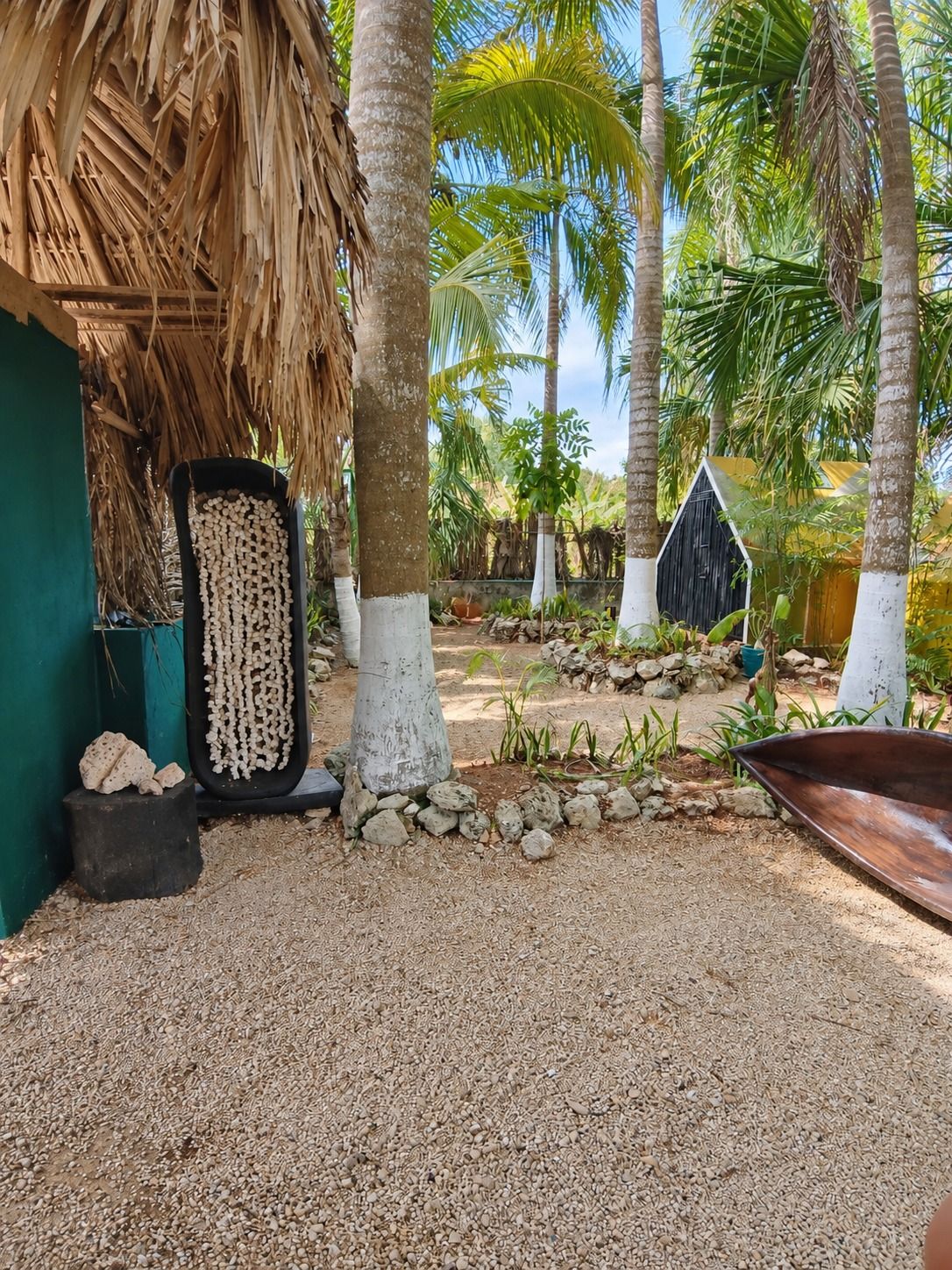 Een tropische tuin met palmbomen, een rieten dak en een klein houten huis.