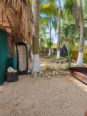 A tropical garden with palm trees, a thatched roof structure, and a small wooden house.