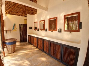 A hotel bathroom with a long vanity, wooden paneling, and a thatched roof. - Reset Retreats (Buenavista)