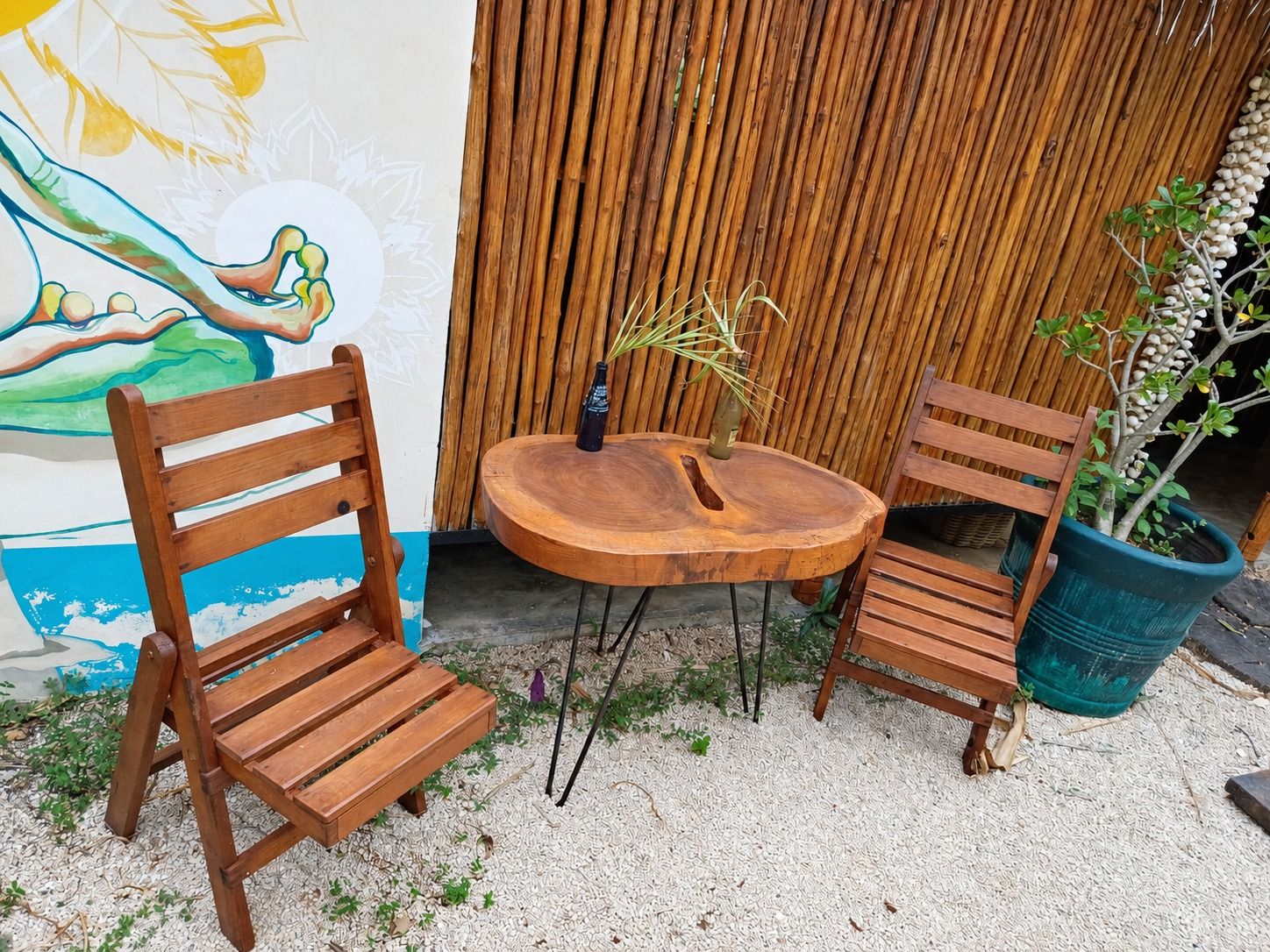A wooden bench and table set against a wall with a mural, surrounded by potted plants.