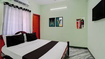 A hotel room with a bed, a red door, a ceiling fan, an air conditioner, and a flat-screen TV mounted on the wall.