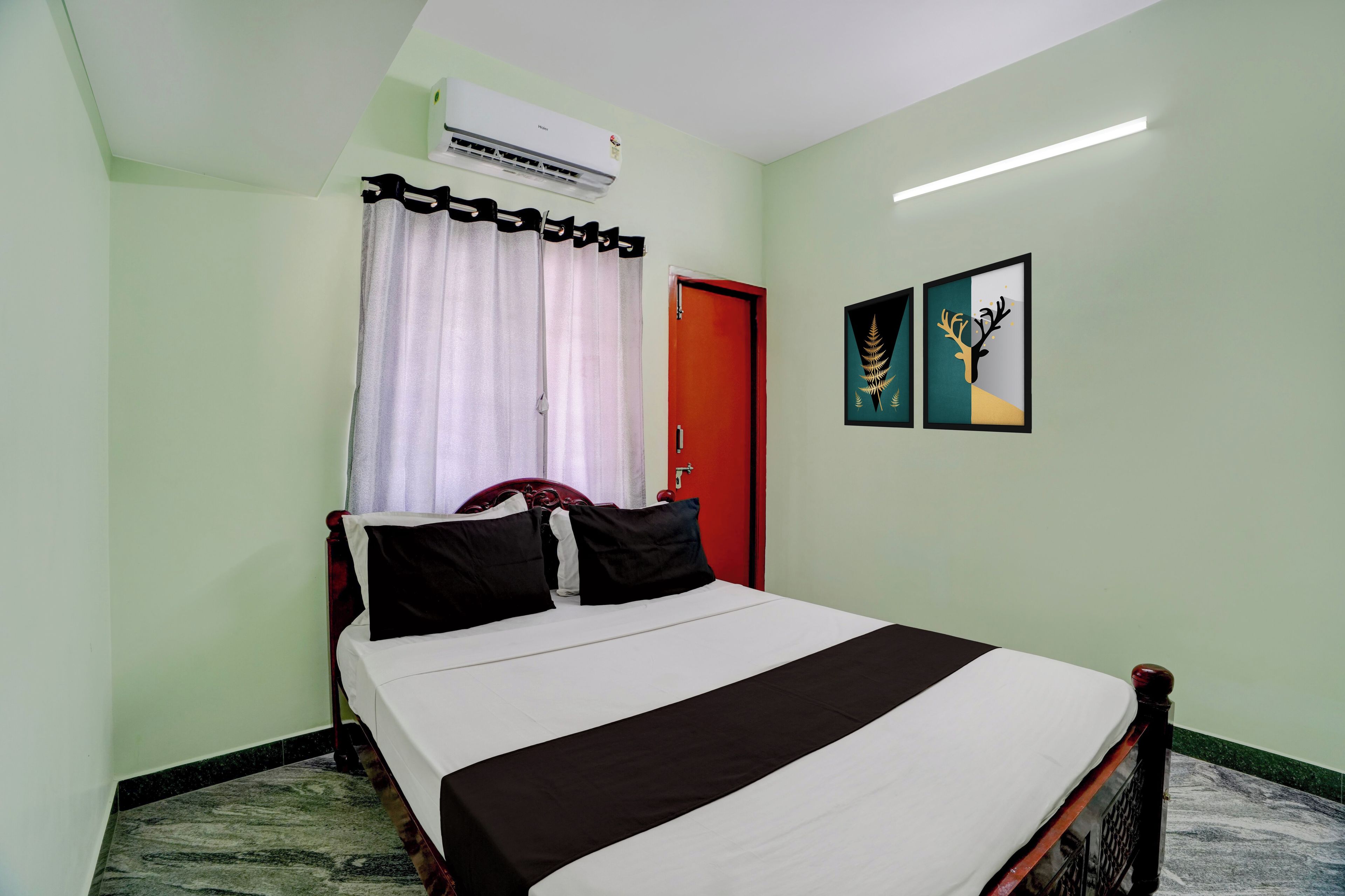 A bedroom with a bed, a red door, an air conditioner, and two framed pictures on the wall.