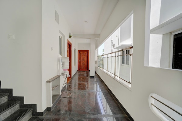 A corridor with a marble floor, white walls, and a wooden door at the end.