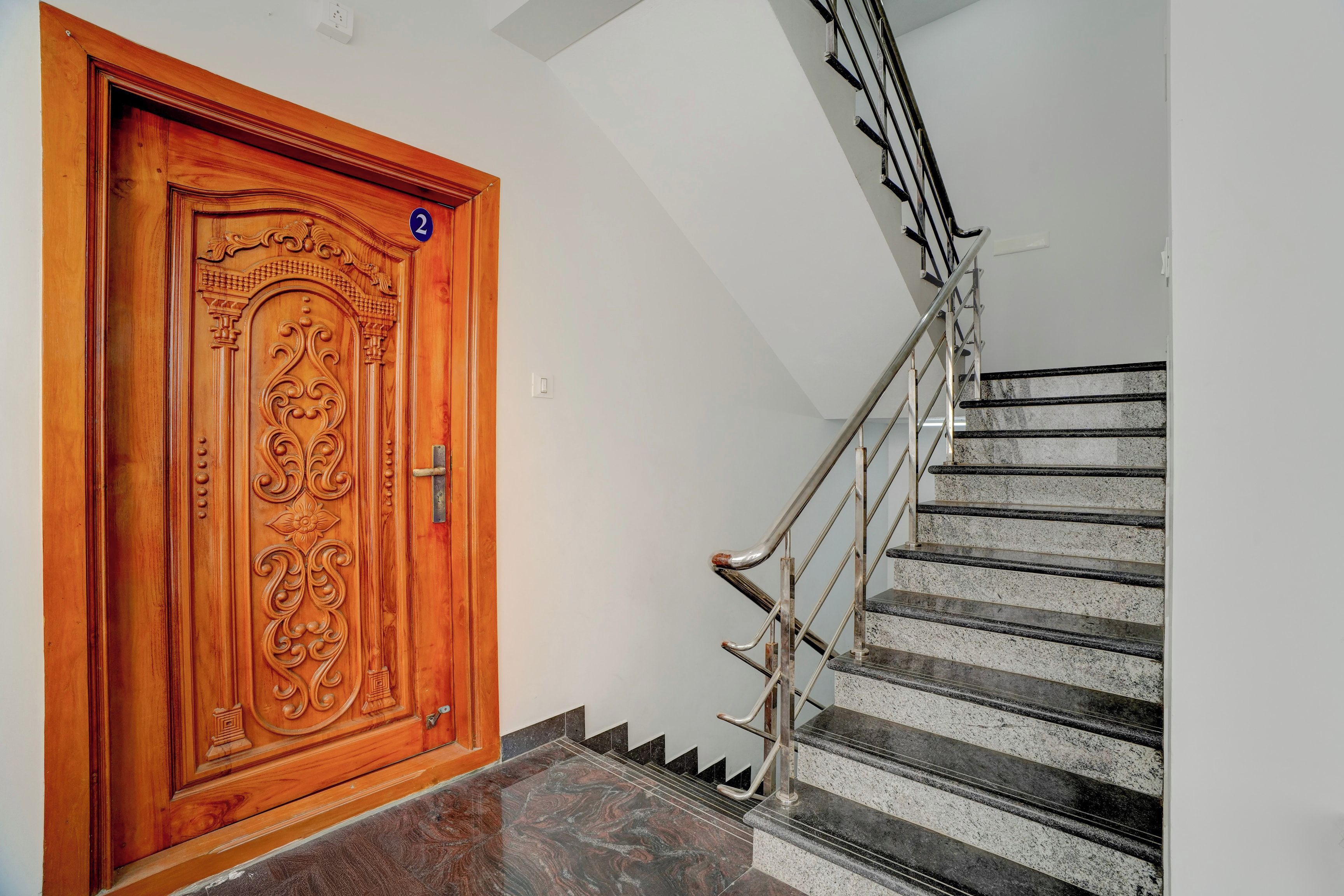 Una puerta de madera con tallas detalladas y una escalera de metal con barandilla.
