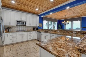 A kitchen with white cabinets, granite countertops, a stainless steel refrigerator, and a built-in microwave. - The Oasis - Seven Bedroom Oceanfront Home with a Private Pool and Hot Tub (Myrtle Beach)