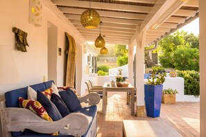 Een overdekt terras met een bank, tafel en potplanten.