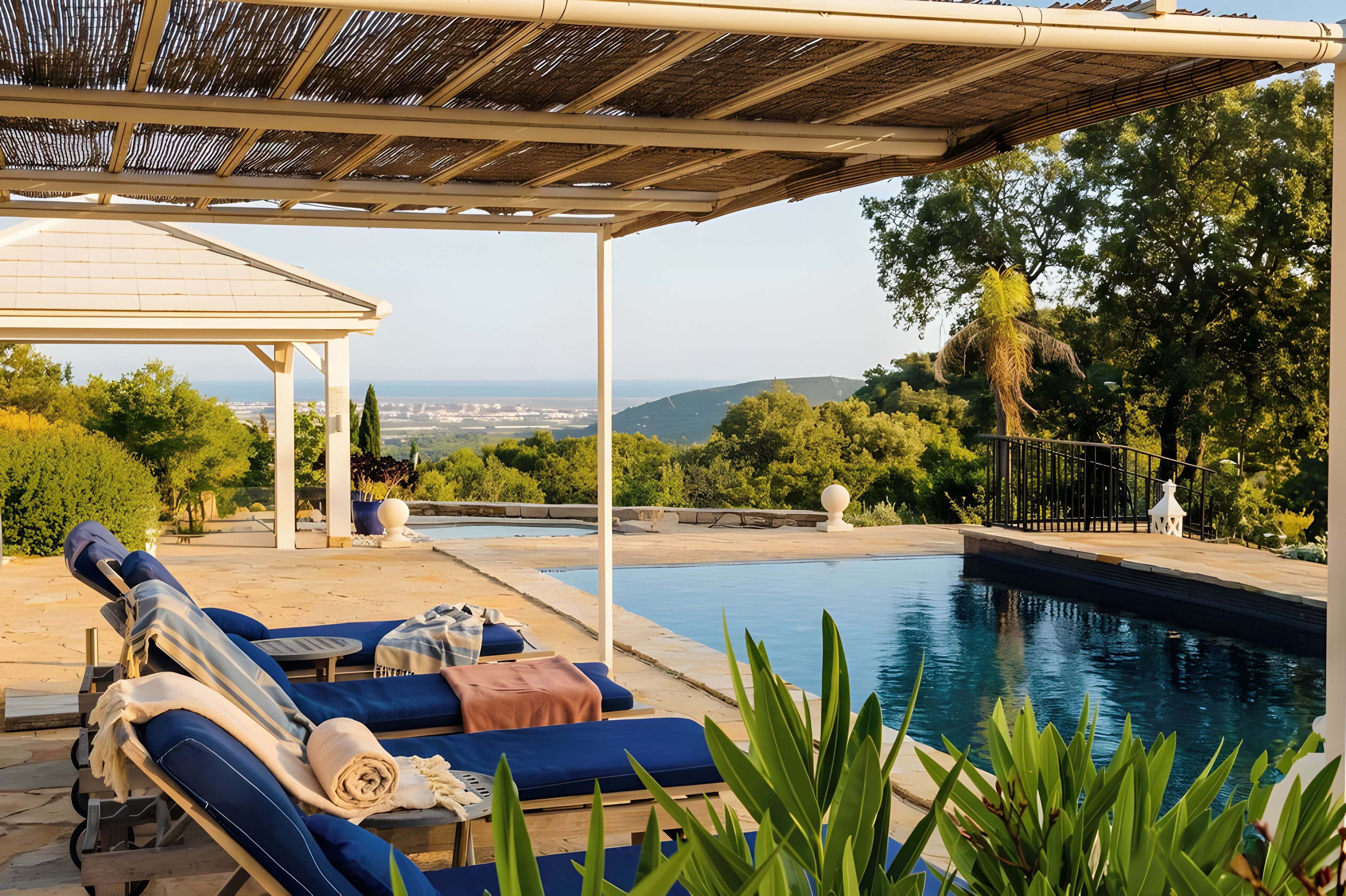 Un área junto a la piscina con sillones de descanso, una pérgola y vistas del paisaje.