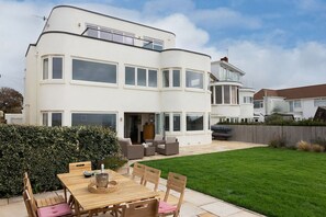 A two-story house with a patio area, a dining table with chairs, and a well-maintained lawn. - 5BR Beachfront Escape with Panoramic Sea Views (Middleton on Sea)