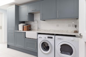A modern kitchen with grey cabinets, a built-in oven, a microwave, and a washing machine. - 5BR Beachfront Escape with Panoramic Sea Views (Middleton on Sea)