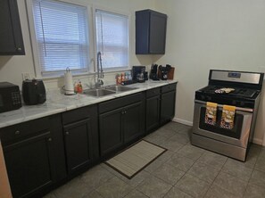 A kitchen with dark cabinets, a stainless steel stove, a sink, and a window with blinds. - Perfect 2-bedroom house in Detroit for a relaxing stay (Detroit)