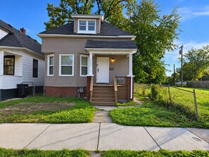 A two-story residential house with a front porch, a small front yard, and a sidewalk leading to the entrance. - Perfect 2-bedroom house in Detroit for a relaxing stay (Detroit)