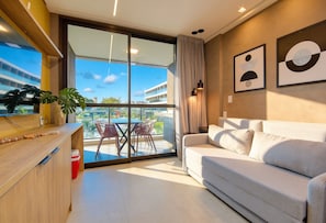 Uma sala de estar moderna com um sofá, uma mesa de jantar com cadeiras, uma janela grande com vista para um edifício e piscina, e obras de arte na parede.