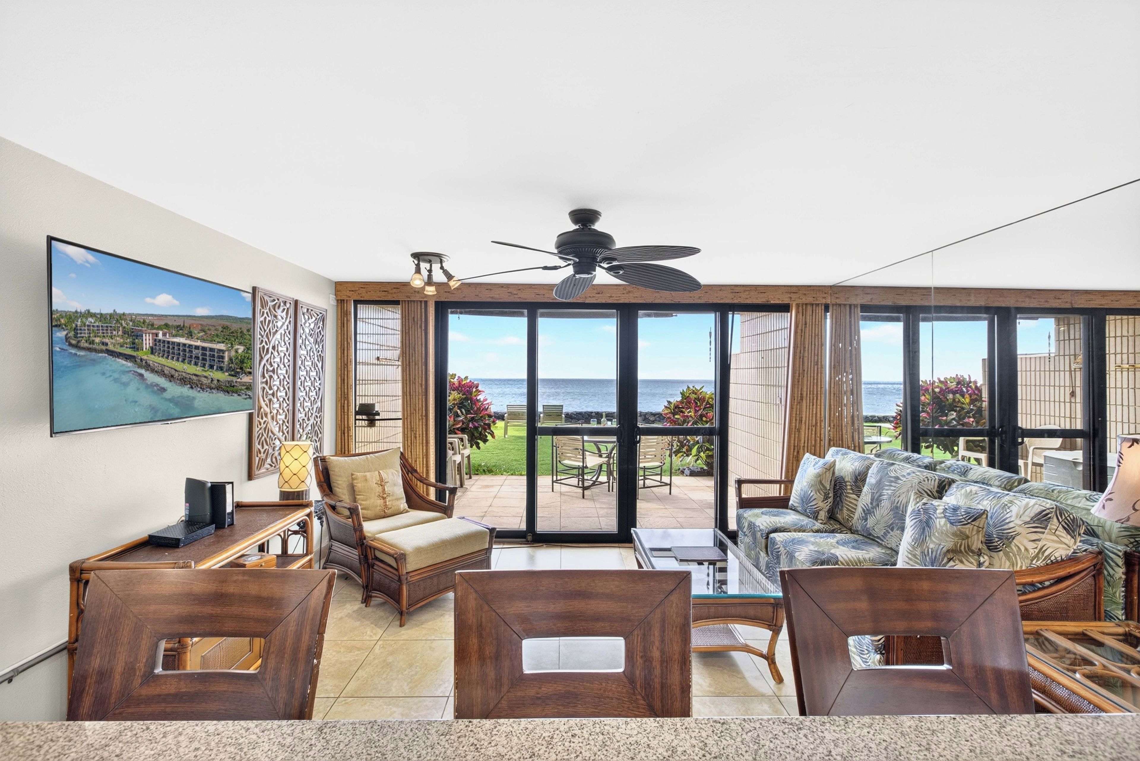 A spacious living room with a large window, a ceiling fan, and a view of the ocean.