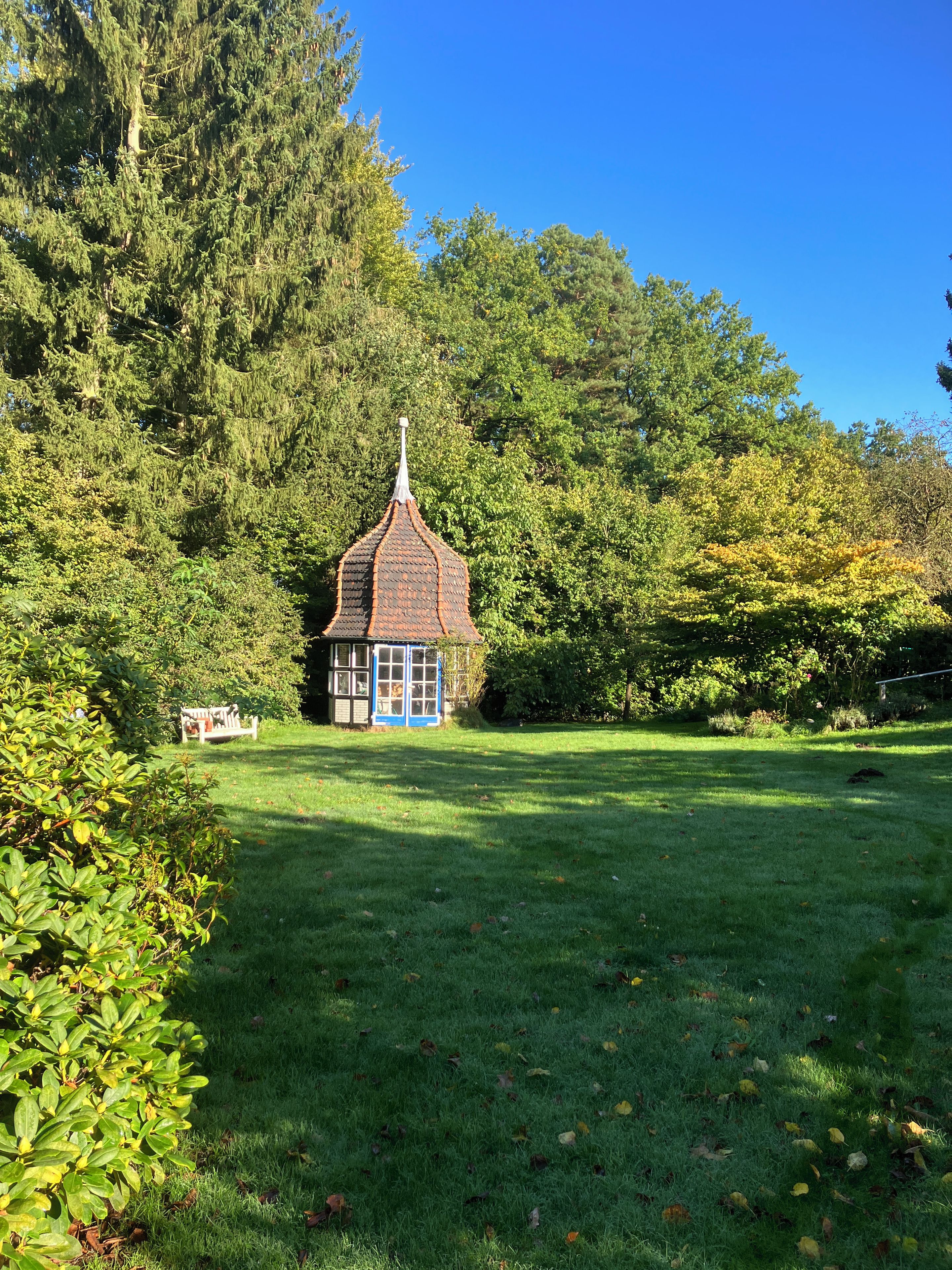 A small, traditional-style building with a tiled roof, surrounded by lush greenery and trees.