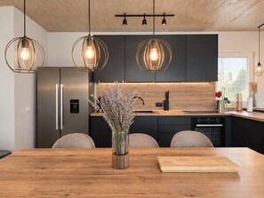 A modern kitchen with a central island, pendant lighting, and a vase of dried flowers. - Holiday House Mountain View Retreat (Kršan)
