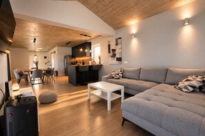 A modern living room with a sofa, a dining area with chairs, a kitchen with a bar, and a ceiling with exposed beams. - Holiday House Mountain View Retreat (Kršan)