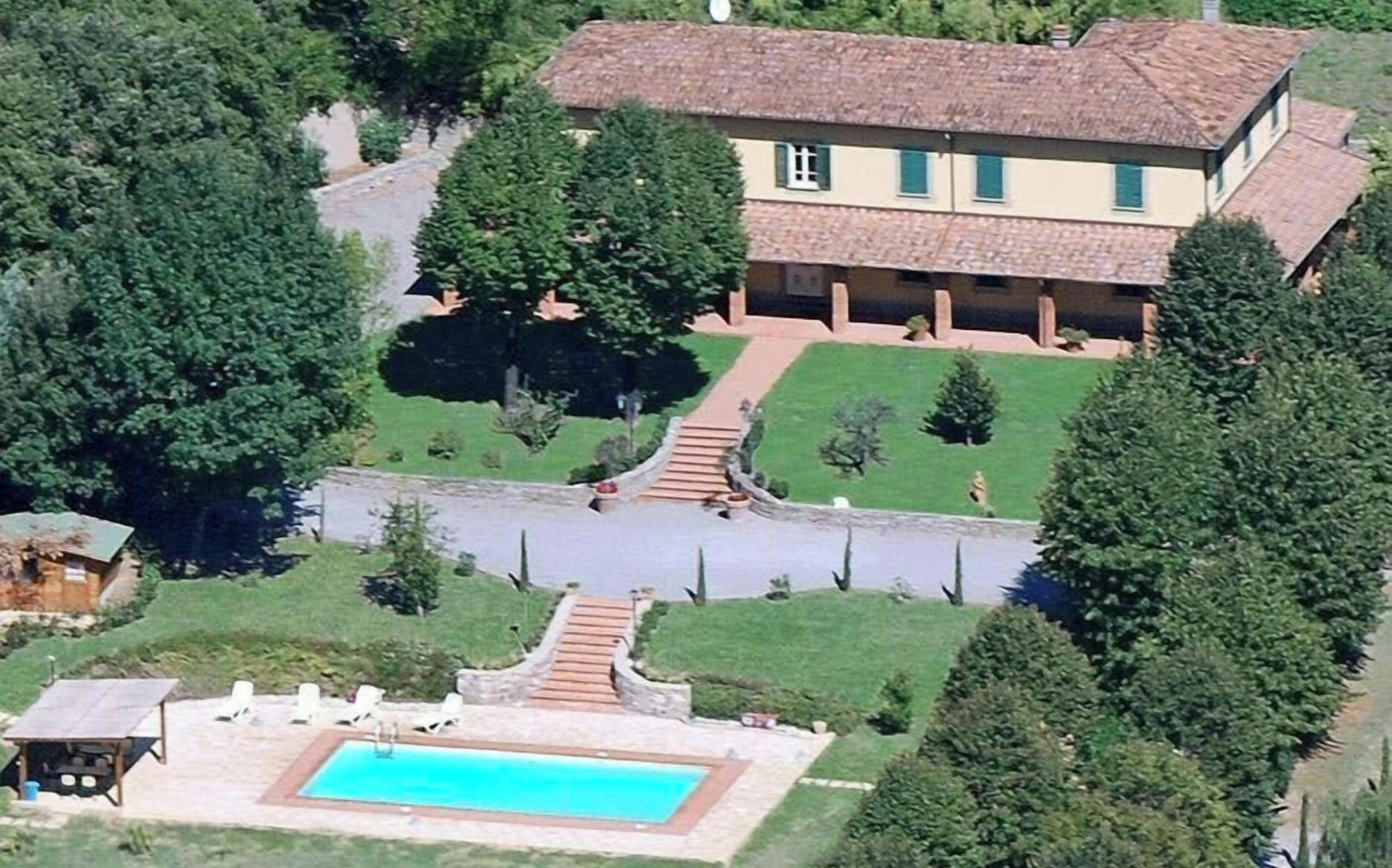 Una casa a due piani con piscina, immersa tra alberi e un prato curato.